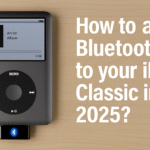 iPod Classic negro con adaptador Bluetooth conectado, mostrando una canción en reproducción sobre una mesa de madera clara